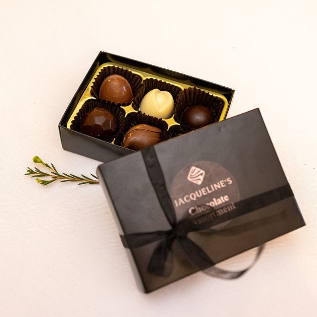 box of six luxury chocolates from jacquelines chocolates with lid propped against it