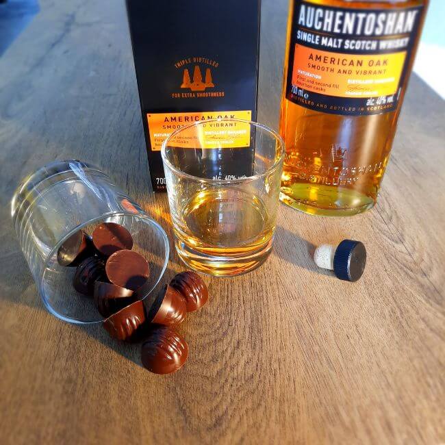 Luxury Chocolate Drawer Box truffles spilling from a glass on it's side next to a bottle of single malt whisky